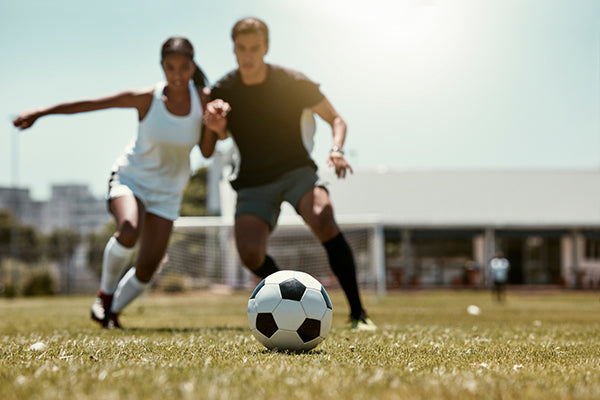 Man and a Woman on a soccer field competing for the ball