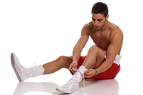 Boxer in red trunks tying shoe on a white background